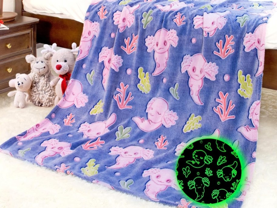 purple color blanket with pink Axolotls on it hanging off a bed and toys to the side
