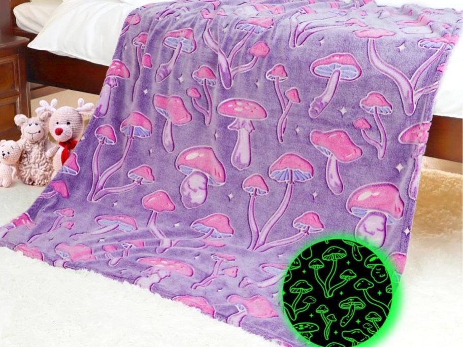 purple blanket with pink mushrooms hanging off a bed, toys next to it