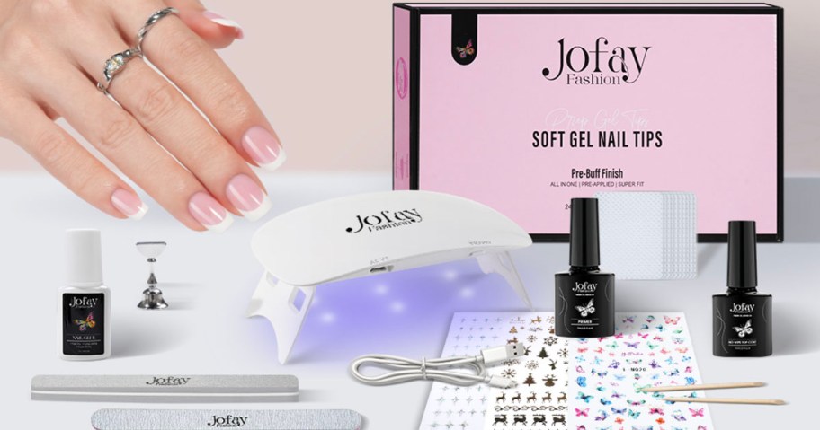 hand with press on nails with joyfay accessories on table including box, primer, top coat, stickers, uv lamp and more