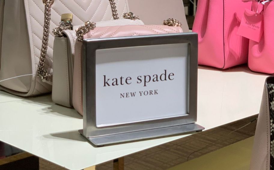 a kate spade table top sign on a display table with hand bags in a kate spade outlet 