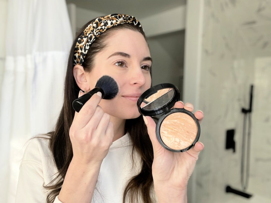 woman applying laura geller baked foundation with a black brush