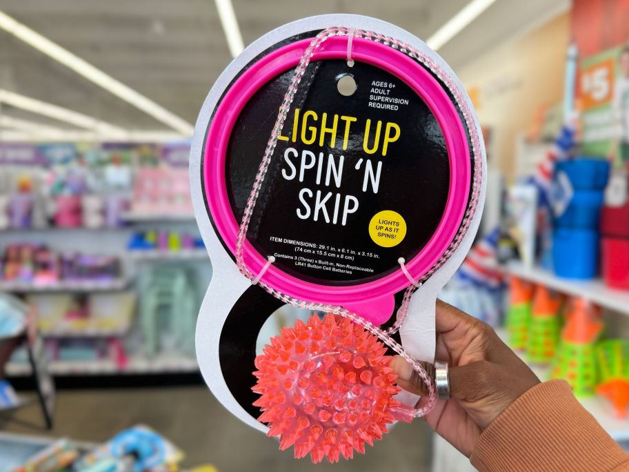 a womans hand holding a a pink light up spin and skip toy