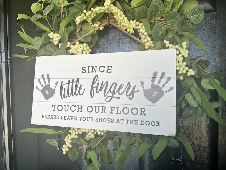 close up of little fingers baby sign on green wreath on front door