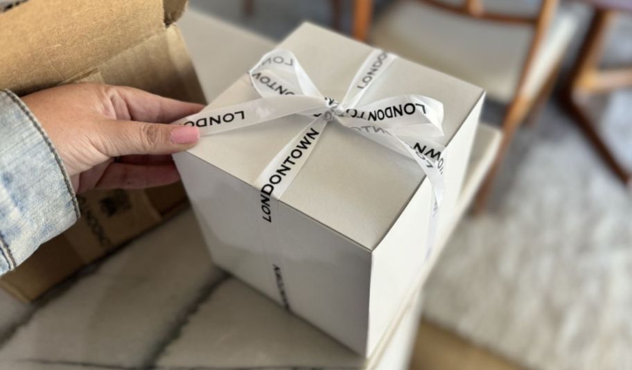 womans hand untying a ribbon around a white cube shaped box