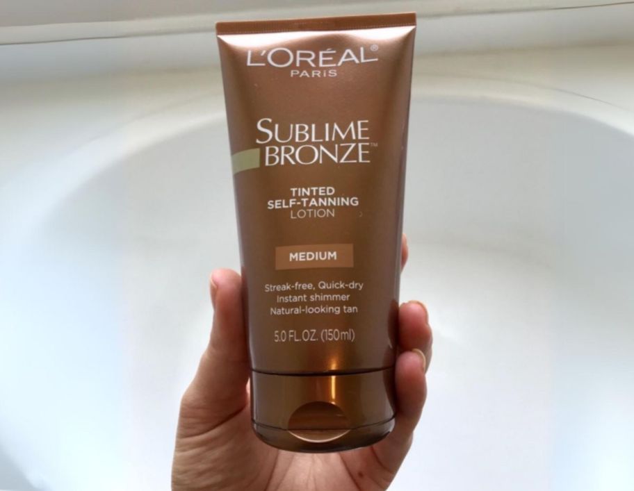a womans hand holding a tube of loreal sublime bronze self tanner in medium
