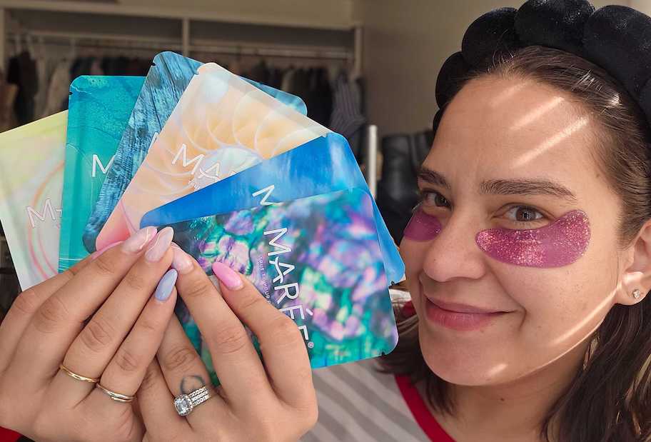 woman holding packs of maree eye gels while wearing pink glitter ones on face