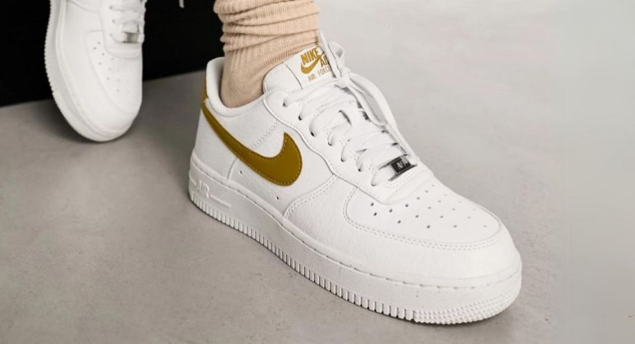 a womans foot in a nike air force 1 sneaker in white and bronze brown