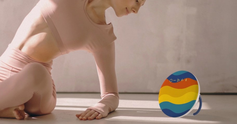 woman doing yoga next to a colorful round bluetooth speaker