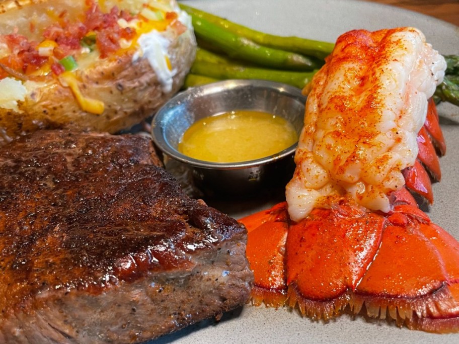 lobster on plate next to steak, butter, and baked potato
