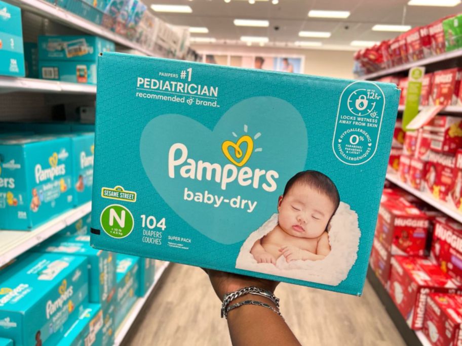 box of pampers diapers being held up by hand in store aisle