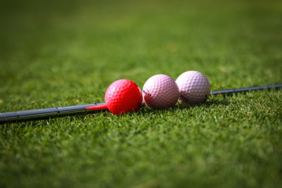 a set of pink golf balls next to a golf club