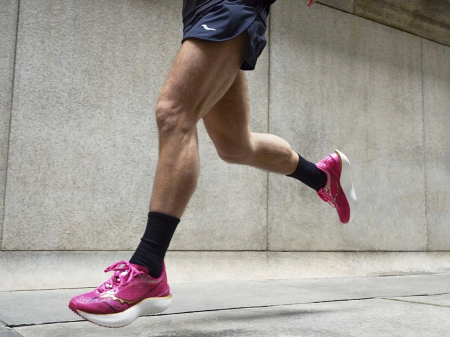 man wearing black shorts and pink running shoes running down sidewalk