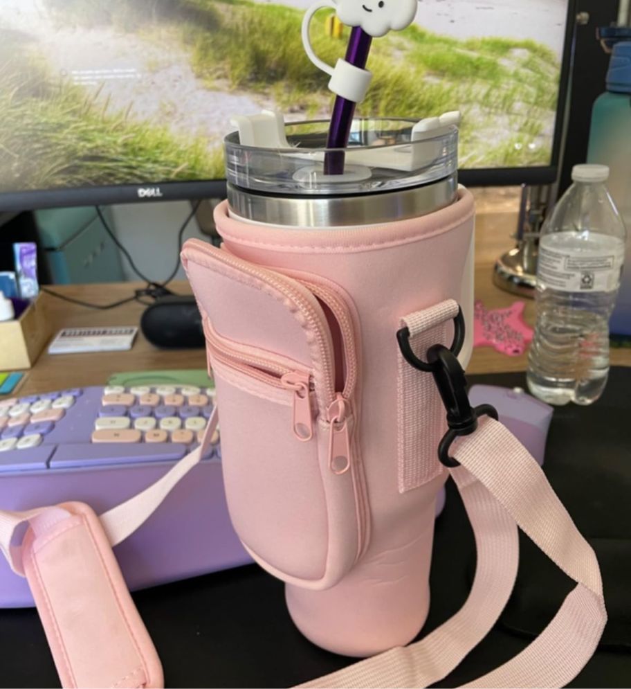 a stanley cup in a bottle sling sitting on desk in front of a computer