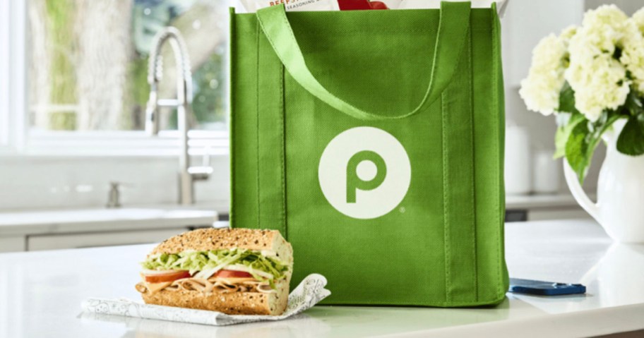 green reusable publix bag with half a sub sitting in front of it on table
