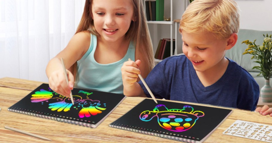 girl and boy coloring in scratch art notebooks at table