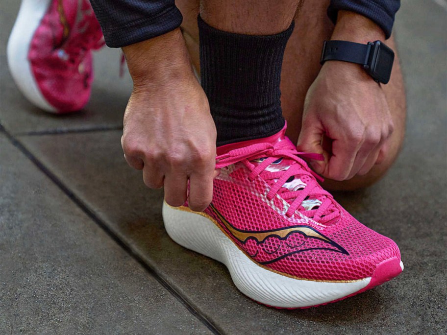 person tying pink saucony shoes on feet