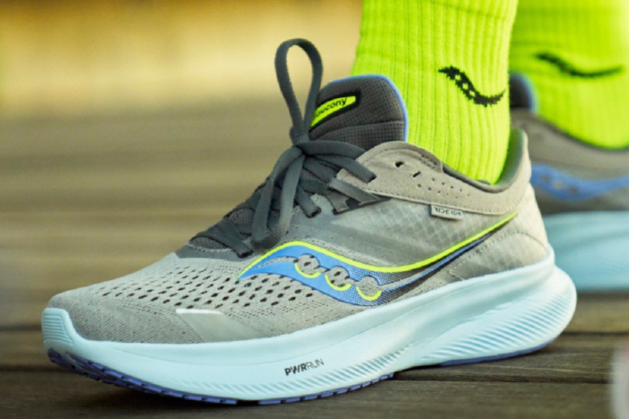 person wearing a gray and blue saucony ride 16 sneaker and a neon green sock