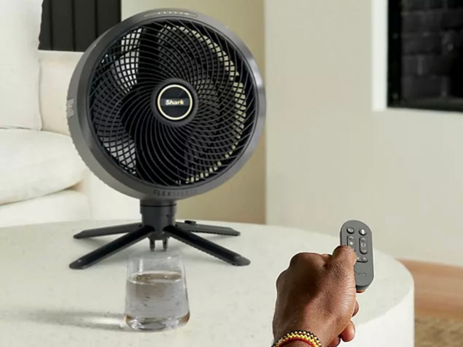 black fan sitting on table top with hand controlling with remote