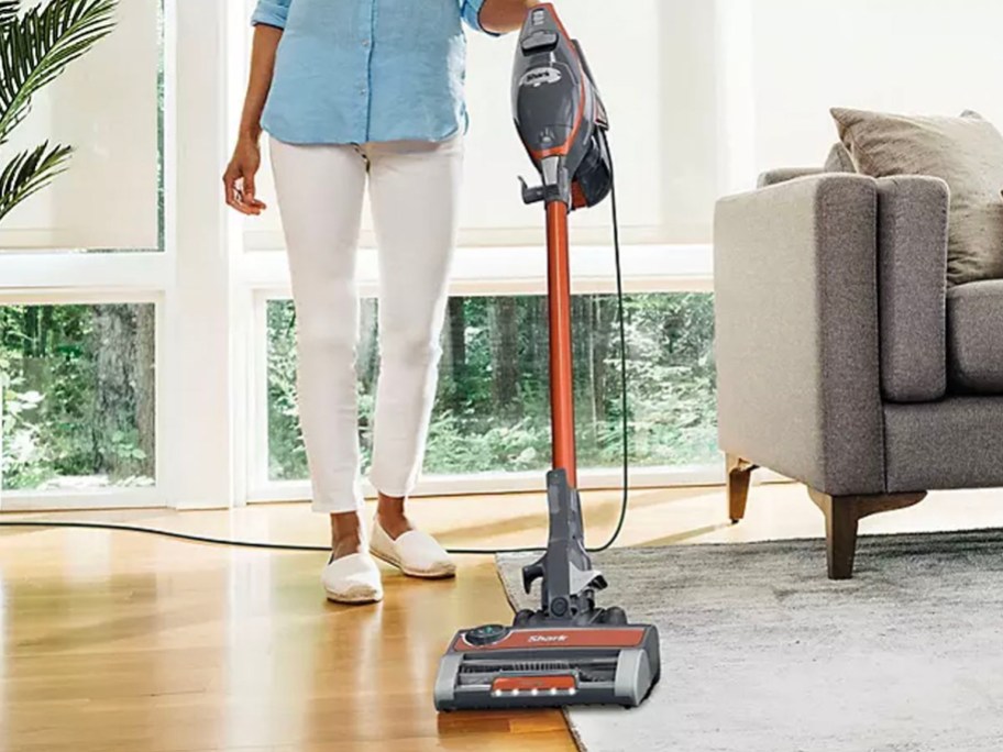woman using gray and orange shark vacuum in living room 