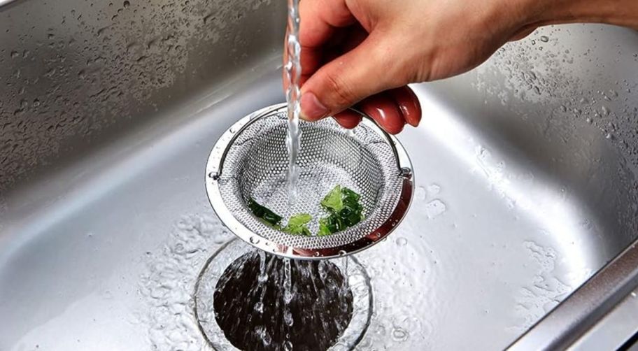 a persons hand holding the handle of a sink drain strainer basket
