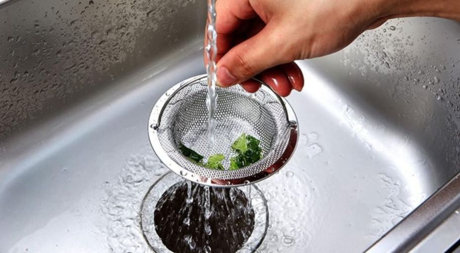 a persons hand holding the handle of a sink drain strainer basket
