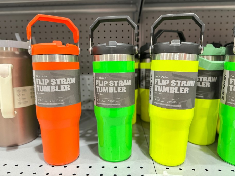 neon orange, green and yellow Stanley Tumblers with handles on shelf