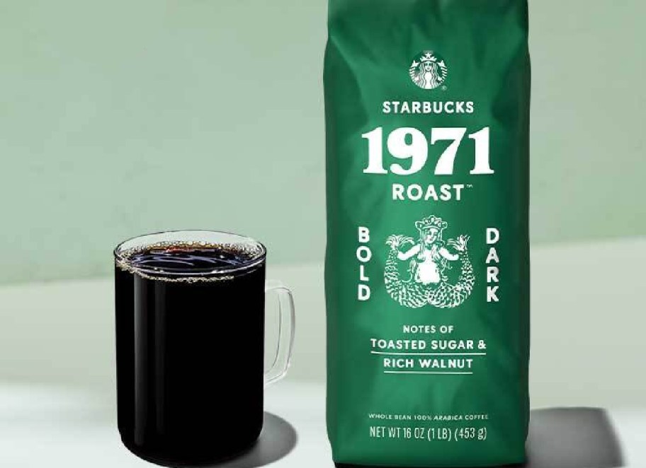 A green bag of starbucks coffee next to a glass mug of coffee.