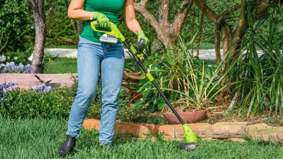 a woman using a weed trimmer next to a flower bed