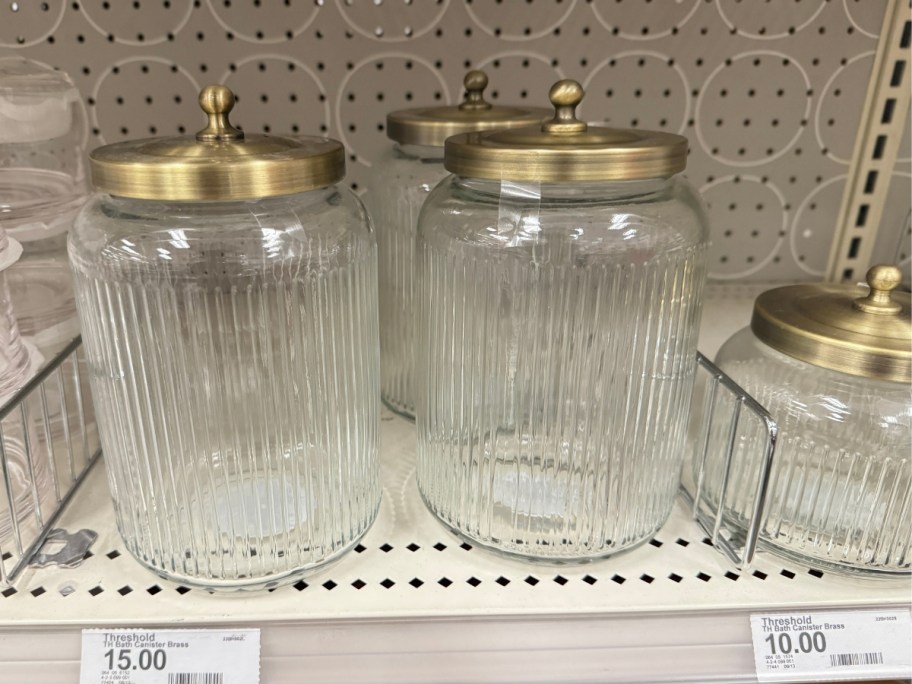 Large and small ribbed glass canisters with gold brass lids on store shelf