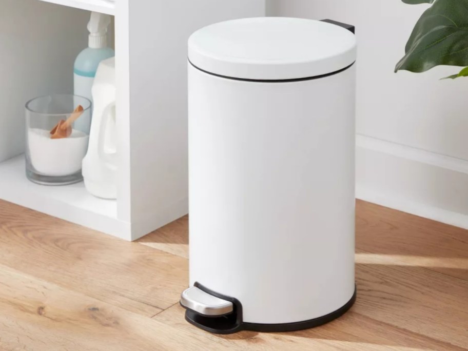 small, white, round, metal step trash can in a bathroom