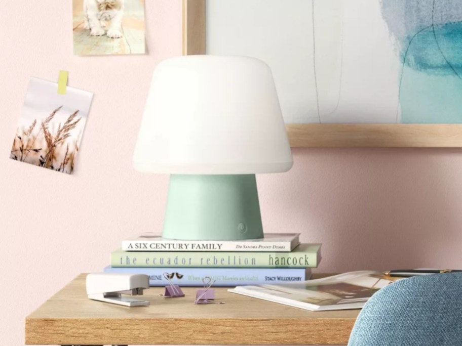 small mushroom style lamp with green base and white top sitting on a stack of books on a desk