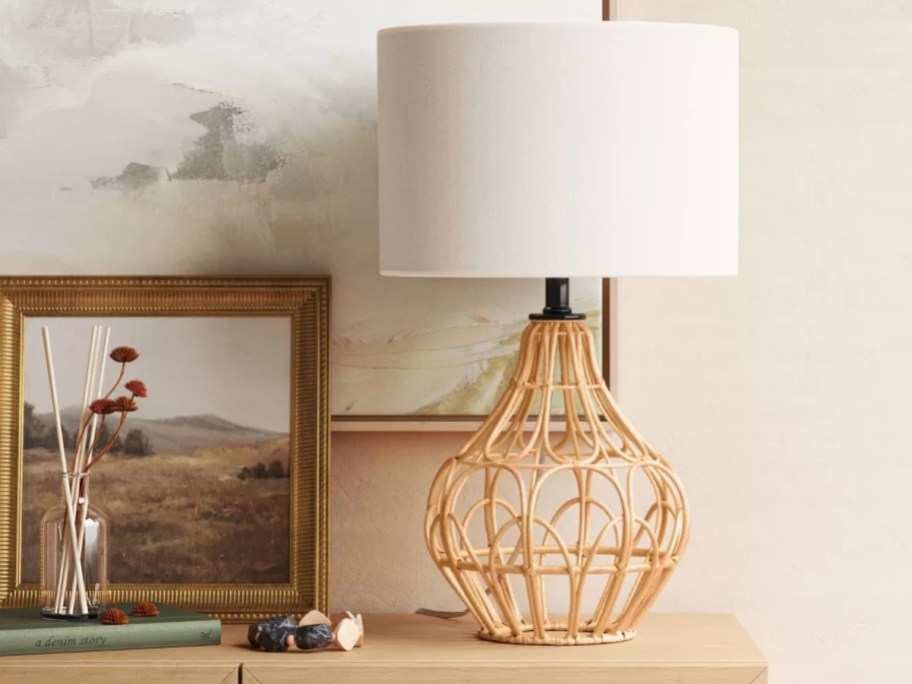 boho rattan style table lamp with white shade sitting on a console table