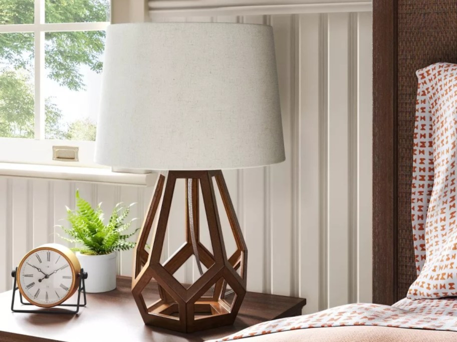 table lamp with wood geometric base and white shade on a bedside table