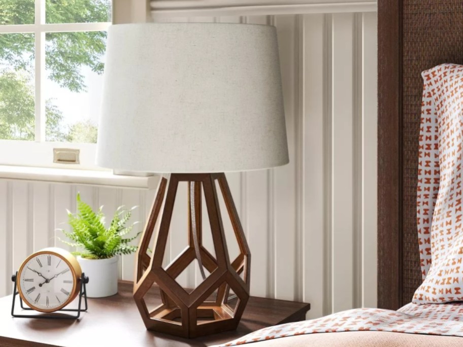 table lamp with wood geometric base and white shade on a bedside table