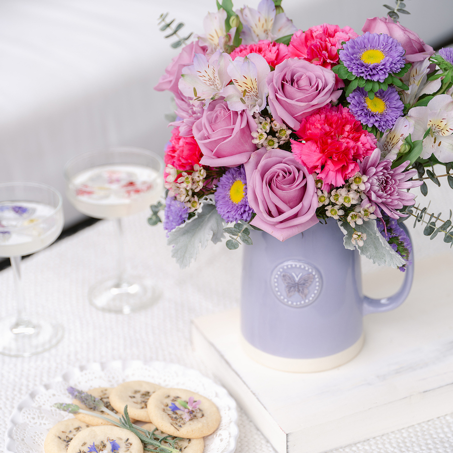 bright pink and purple bouquet of flowers in purple vase on table with cookies and cocktails