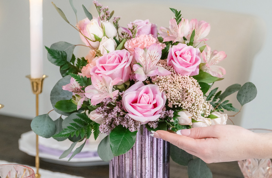 hand touching edge of teleflora pink and green bouquet of flowers