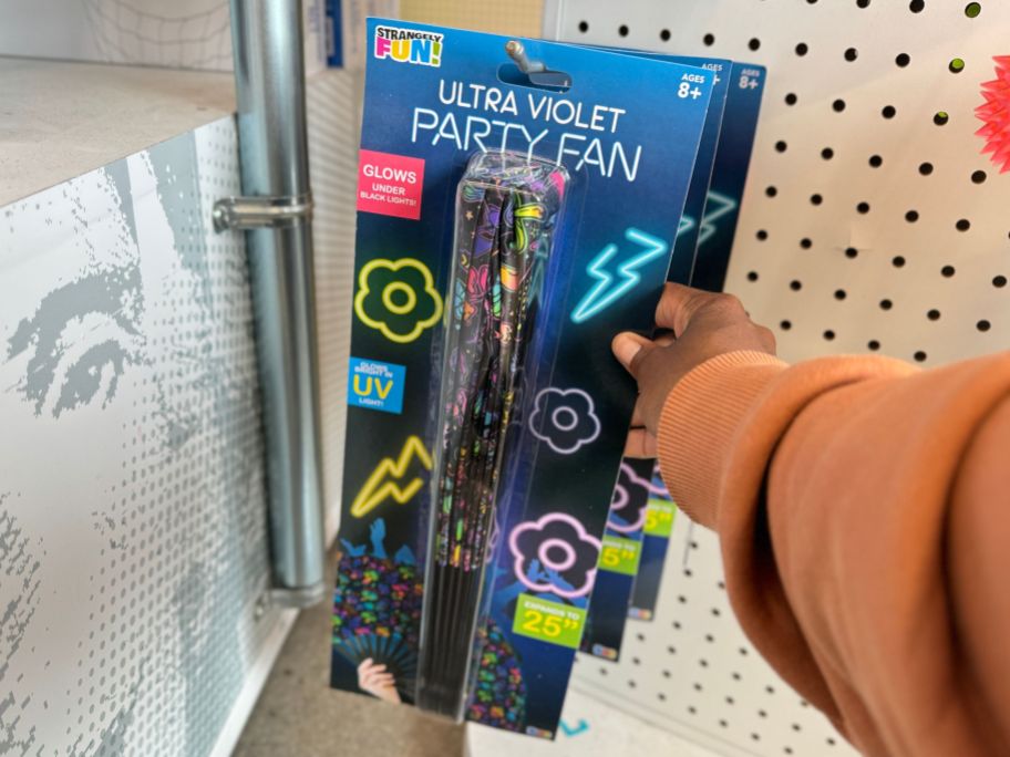 a womans hand grabbing a uv party fan from a peg on a store aisle