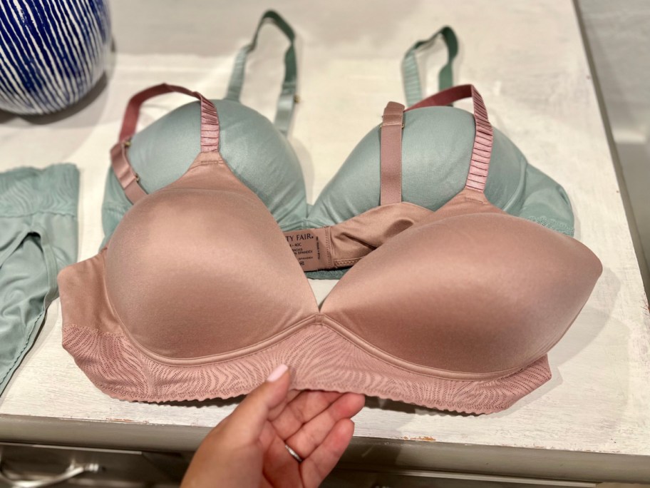 hand holding light blush and light teal bras