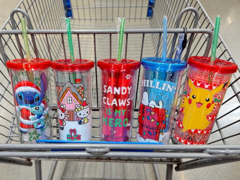 plastic tumblers with straws and lids that have characters in Christmas styles on them - Pikachu, Stitch, Jack Skellington, Hello Kitty and Snoopy - in a Walmart cart