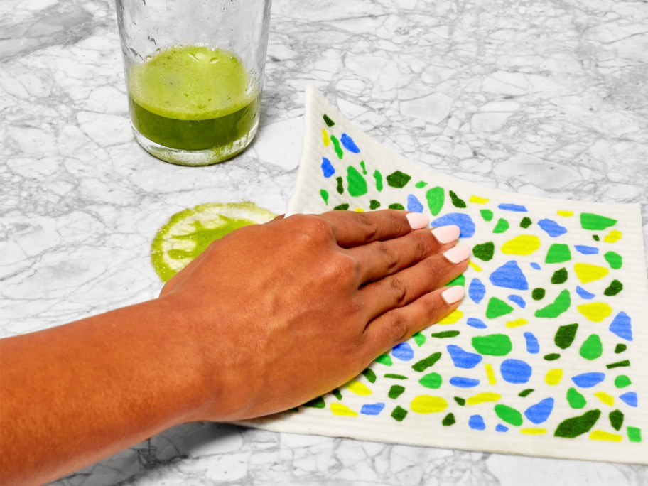 hand using green and blue dishcloth to clean countertop