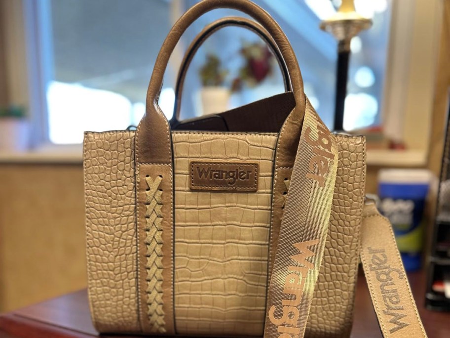tan wrangler purse with strap sitting on table