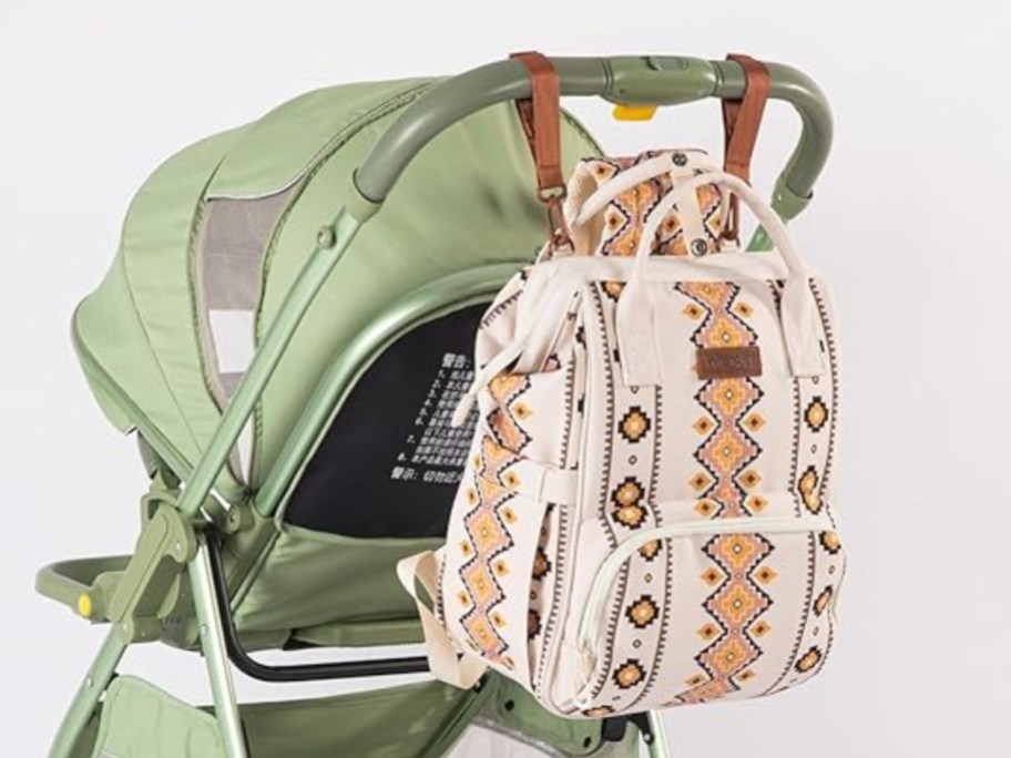 white, tan & brown western print diaper bag backpack hanging on the back of a green stroller