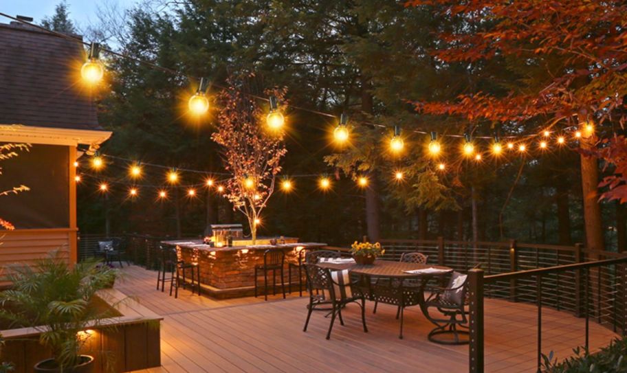 Lit string lights on a deck. Strung above a dining table and bar