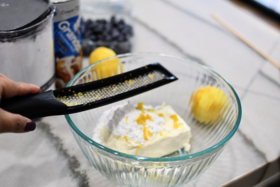 zesting a lemon over a bowl with cream cheese 