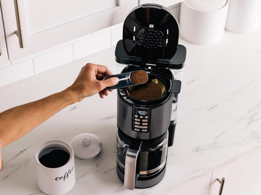person putting scoops of ground coffee into the filter of a Ninja XL coffee maker