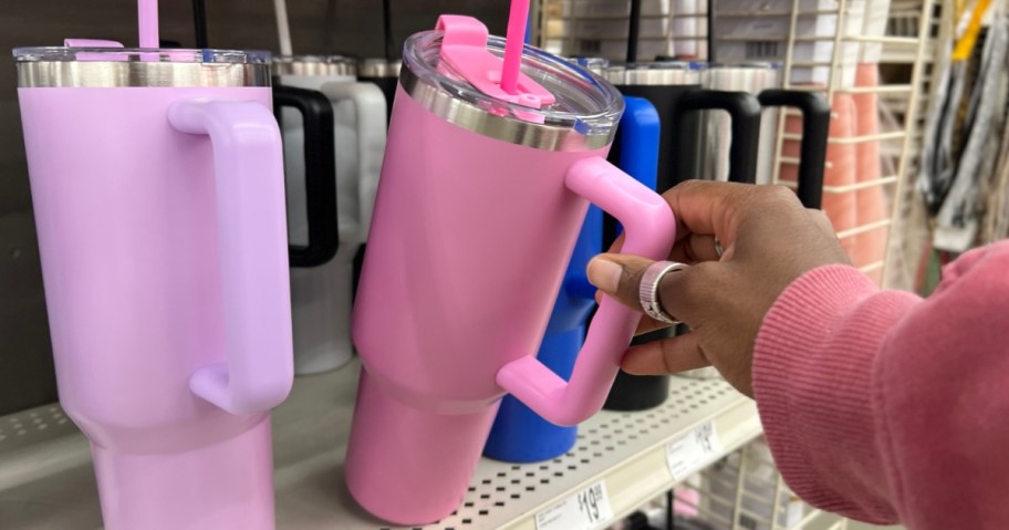 hand reaching for a pink 40oz stainless steel tumbler on shelf with more in other colors