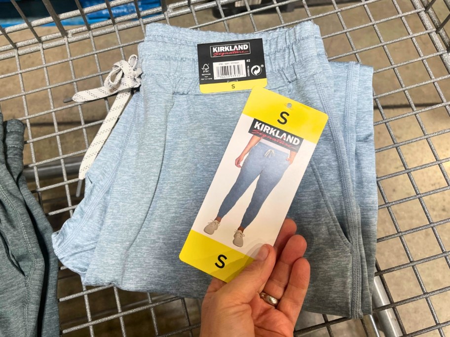 hand holding the tag of a pair of light blue women's joggers that are in a shopping cart