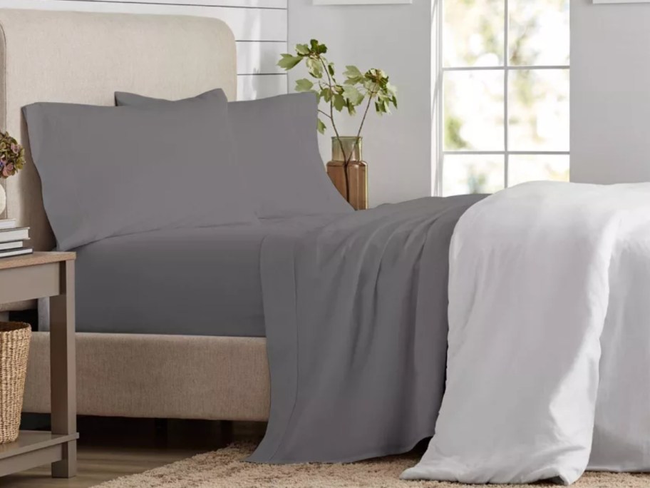bed with comforter pulled back showing grey sheets and pillows