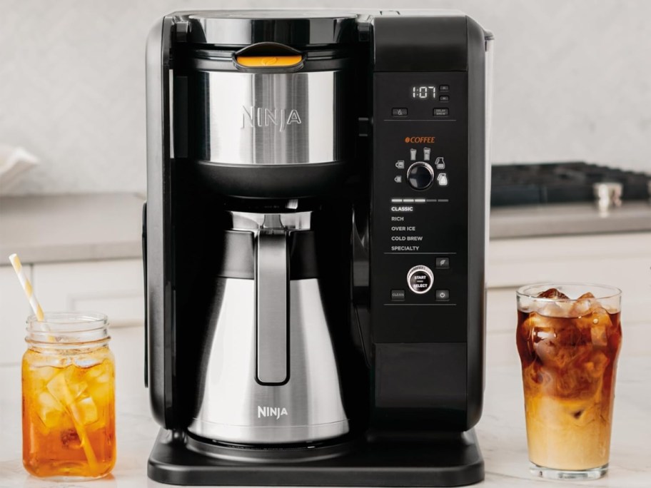 large black and stainless steel Ninja coffee maker with a stainless steel carafe, cups of iced tea and coffee to the sides