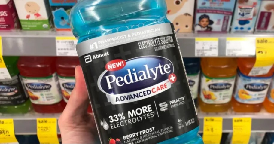 hand holding a bottle of Pedialyte AdvancedCare Plus Berry Frost with more kid's items on store shelves behind it